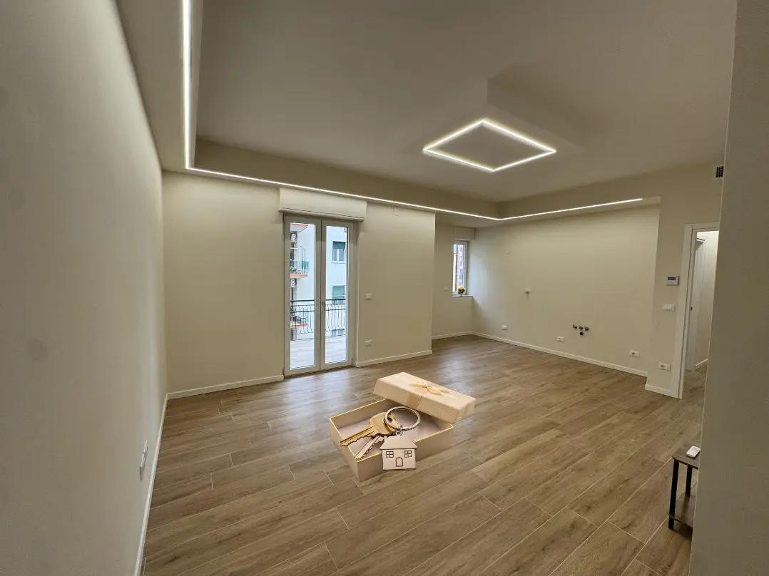 Soggiorno ristrutturato con parquet e luci a LED, con le chiavi della nuova casa in una scatola regalo al centro